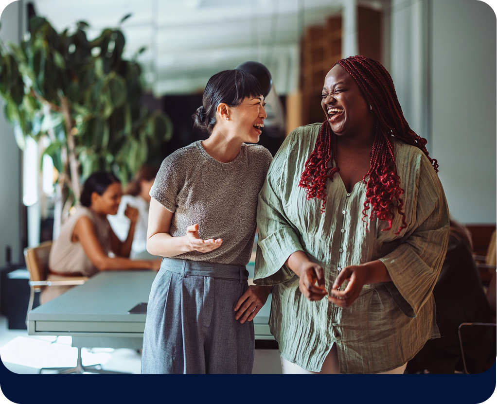 Duas mulheres, em pé, rindo, em escritório